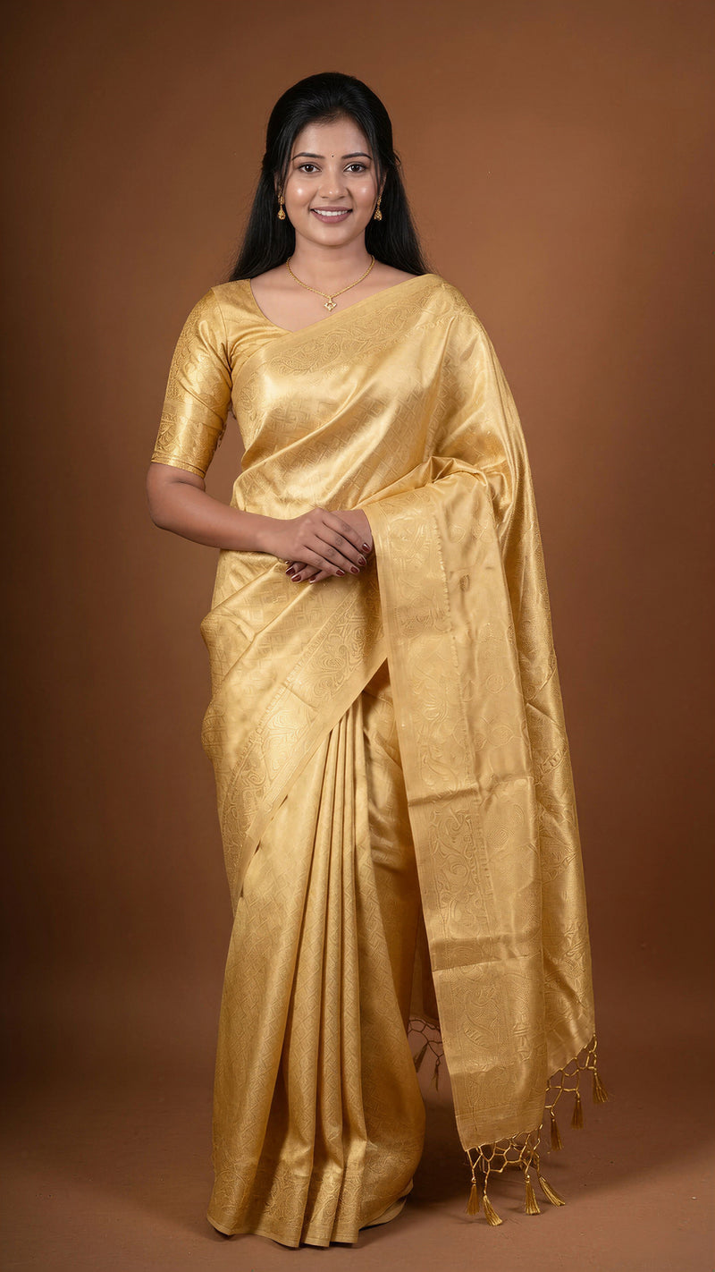 A woman modeling a golden metallic silk saree with a matching short-sleeve blouse against a solid brown studio background.