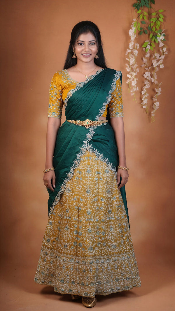 A woman modeling a traditional Indian saree with a yellow and green color-blocked design, featuring intricate gold embroidery and a matching embroidered blouse, set against a warm brown studio backdrop.