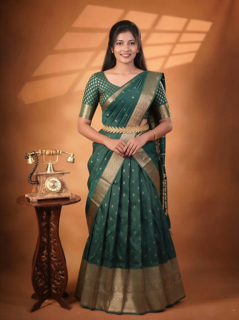 A woman wearing a dark teal green saree with gold zari borders and motifs, standing next to a vintage wooden table with a rotary telephone against a warm brown studio backdrop.