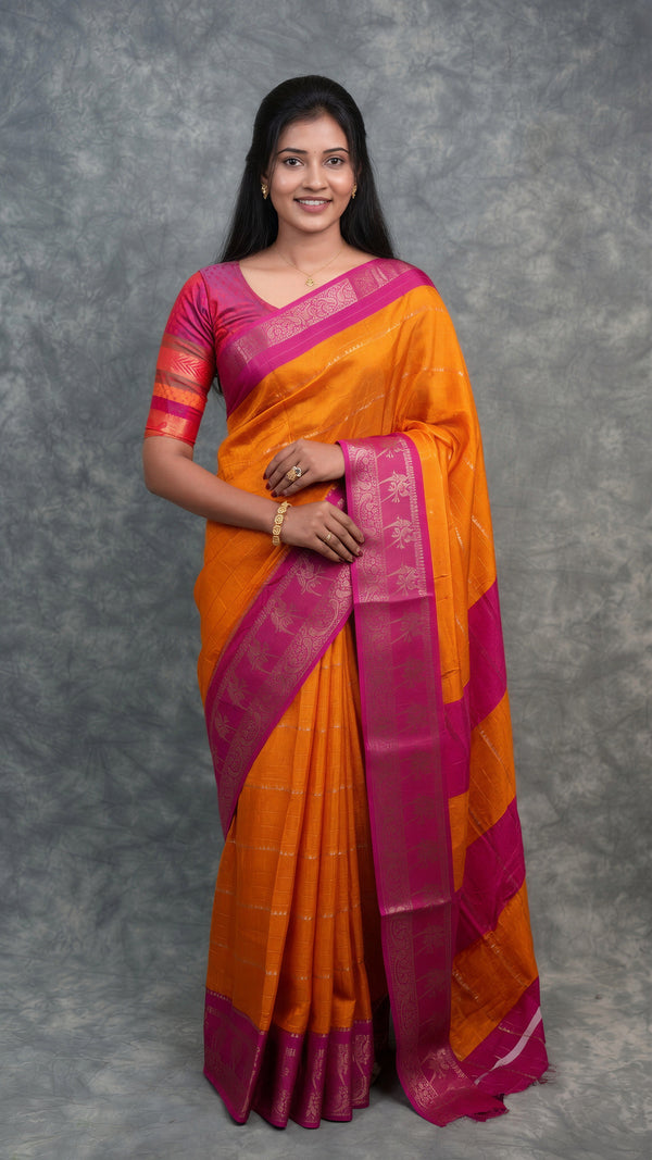 A woman modeling a bright orange and magenta striped silk saree with a metallic gold border, standing against a textured gray studio backdrop.