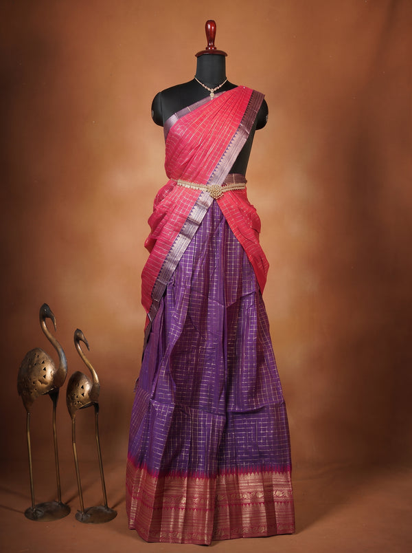 A traditional Indian saree displayed on a black mannequin torso against a warm brown studio backdrop. The saree has a bright pink upper section and a purple lower section with gold woven detailing, draped elegantly with a matching pink and purple border.