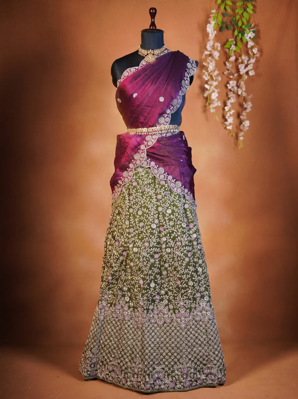 A traditional Indian lehenga choli dress displayed on a black mannequin. The garment features a rich magenta and purple draped blouse (choli) with intricate silver embroidery, paired with a heavily embellished green and silver embroidered skirt (lehenga).