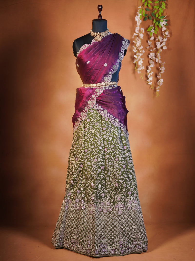 A traditional Indian lehenga choli dress displayed on a black mannequin. The garment features a rich magenta and purple draped blouse (choli) with intricate silver embroidery, paired with a heavily embellished green and silver embroidered skirt (lehenga).